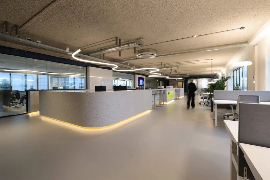 Moderne receptiebalie met terrazzo-look en een golvende lichtinstallatie aan het plafond, onderdeel van een strak en toekomstbestendig kantoorontwerp.