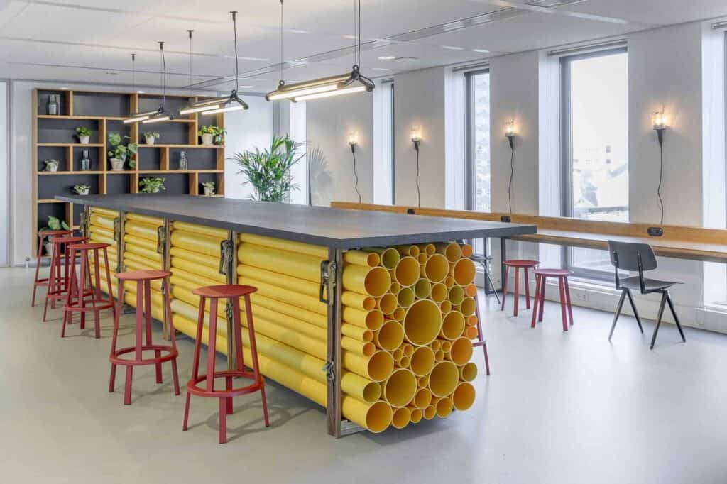Opvallende hoge vergadertafel met een onderstel van hergebruikte gele buizen als statement in een moderne werkomgeving in Tilburg.